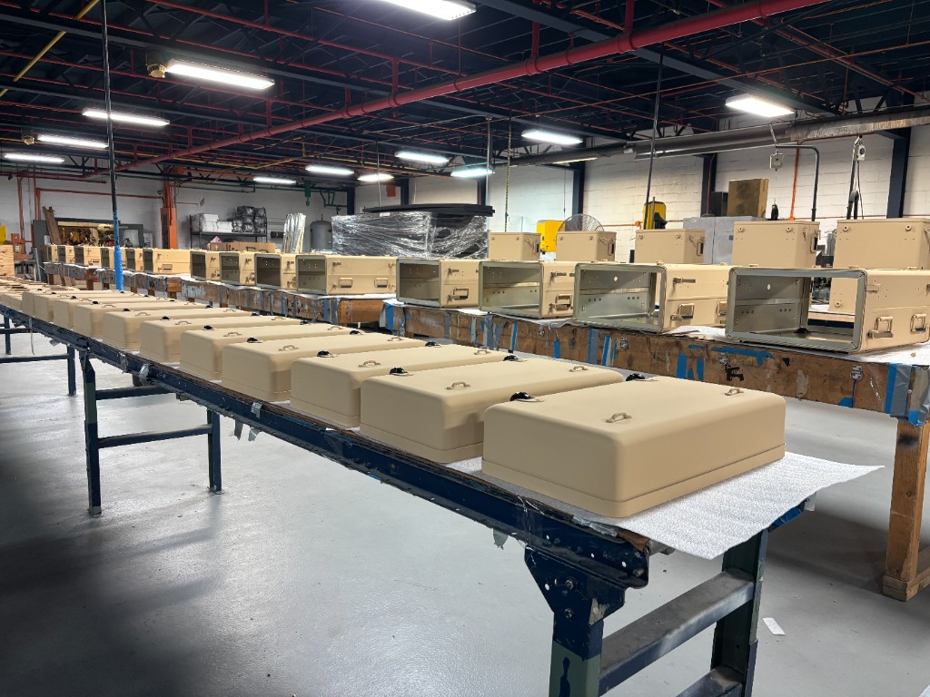 Skydyne production floor with tan MIL-SPEC CARC rackmount cases and lids staged on assembly lines